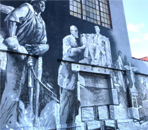A man chisels, a man looks at Lincoln statue model, and a woman descends a staircase